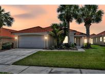 Charming home featuring a red tile roof, palm trees, and a well-manicured lawn against a colorful sunset sky at 112 Cordova Ave, Davenport, FL 33897