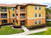Bright condo building featuring yellow and orange tones, complemented by lush landscaping and palm trees at 5447 Vineland Rd # 1308, Orlando, FL 32811