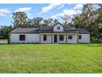 Charming single-story home featuring a modern farmhouse design with a large front yard and wooden porch columns at 13393 Sw 484 Hwy, Ocala, FL 34481