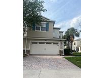 Two-story tan home with a large two-car garage and brick paver driveway at 1122 Priory Cir, Winter Garden, FL 34787