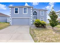 Two-story home featuring blue stucco exterior, two-car garage, and concrete driveway, set against a blue sky at 125 Vervain Ave, Davenport, FL 33837