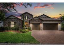 Charming stone home featuring a three-car garage, brick paver driveway and lush landscaping at 16761 Broadwater Ave, Winter Garden, FL 34787