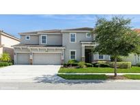 Charming two-story home with a three-car garage, manicured lawn, and mature tree at 7017 Oakwood St, Davenport, FL 33837