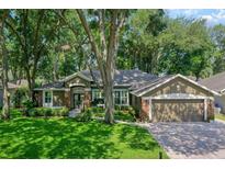 Beautiful single-story home featuring a lush, green lawn and a brick-accented facade with mature tree landscape at 920 Cool Springs Cir, Ocoee, FL 34761