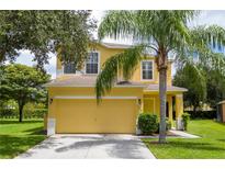 Charming two-story yellow home featuring a palm tree, well-manicured lawn, and a two-car garage at 17614 Woodcrest Way, Clermont, FL 34714