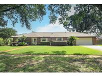 Charming brick single-story home with a well-manicured lawn, mature trees, and attached two car garage at 1529 Ensenada Dr, Orlando, FL 32825