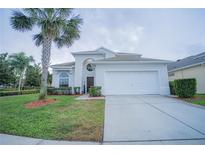 Charming home features a two-car garage, well-maintained landscaping, and a decorative palm tree in the front yard at 8100 Fan Palm Way, Kissimmee, FL 34747