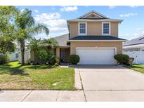 Two-story home with tan exterior, attached two-car garage, driveway, and a landscaped front yard at 2332 Andrews Valley Dr, Kissimmee, FL 34758