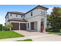 Two-story home with a two-car garage, white exterior, brown tile roof and a brick driveway, complemented by lush landscaping at 11707 Hampstead St, Windermere, FL 34786