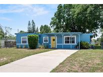 Charming blue single-story home featuring a yellow door, manicured landscaping, and a spacious driveway at 11520 Churchill St, Orlando, FL 32817