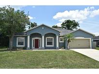 Charming blue home featuring a two-car garage, well-manicured lawn, and covered front entry way at 1947 Vienna Ave, Deltona, FL 32725