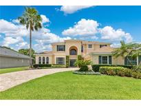 Stunning two-story home featuring lush landscaping, a circular driveway, and a grand entrance beneath a bright blue, cloudy sky at 4221 Kezar Ct, Belle Isle, FL 32812