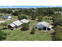 Spacious property featuring a white home with a metal roof and a detached garage, all nestled in a lush green landscape at 4895 Cr 134B, Wildwood, FL 34785
