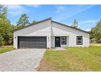 Modern home boasts a gray brick driveway, complemented by a black garage door and a clean, minimalist white exterior at 17762 Sw 33Rd Ter, Ocala, FL 34473
