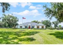 Charming single-story home features a well-maintained lawn, crisp white facade, red door, and lovely shuttered windows at 5478 Nw 153Rd Ct, Morriston, FL 32668