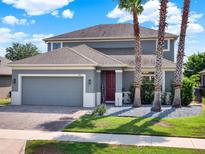 Charming two-story home boasts a gray exterior, paver driveway, and well-manicured landscaping with mature palm trees at 987 Nathan Ridge Rd, Clermont, FL 34715