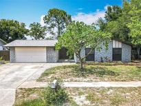 Charming single-story home featuring stone accents, a two-car garage, and mature trees on a sunny day at 7679 Bent Bow Trl, Winter Park, FL 32792