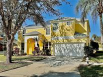 Bright yellow two-story home with a two-car garage and mature landscaping under a clear blue sky at 8520 La Isla Dr, Kissimmee, FL 34747