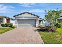 Charming single Gathering home featuring a gray stucco exterior, two-car garage and a brick paver driveway at 29400 Caspian St, Leesburg, FL 34748