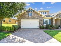 Charming stone home featuring a two-car garage with brick paver driveway and lush landscaping at 4133 Foxhound Dr, Clermont, FL 34711