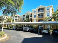 A multi-story apartment building with carport parking featuring screened balconies and lush landscaping under a sunny, blue sky at 6451 Old Park Ln # 407, Orlando, FL 32835