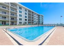 Community pool with blue water, brick perimeter, chairs, and view of the beachside building at 4153 S Atlantic Ave # 2120, New Smyrna Beach, FL 32169