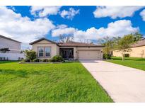 Charming single-story home boasts a lush green lawn and inviting curb appeal with a two car garage and neutral color palette at 16379 Blooming Cherry Dr, Groveland, FL 34736