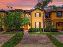Charming two-story townhome featuring a yellow facade, brown accents, and well-manicured landscaping at 3725 Calabria Ave, Davenport, FL 33897