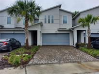 Attractive townhome featuring a two-car garage, modern design, palm trees, and brick paver driveway at 3316 Bellissimo Ave, Kissimmee, FL 34746