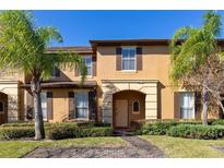 Inviting townhome featuring tan stucco, shuttered windows, a quaint front porch, and lush landscaping at 1022 Calabria Ave, Davenport, FL 33897