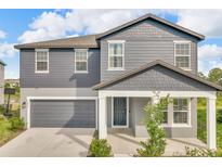 Charming two-story home with blue siding, a gray garage door, and a covered front porch at 2210 Derwent Dr, Davenport, FL 33896