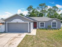 Charming single-story home features a gray exterior, attached garage, well-manicured lawn, and red front door at 3130 Clewiston St, Deltona, FL 32738