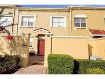 Charming townhome featuring a vibrant red front door, lush landscaping, and textured tan facade at 2398 Bella Vista Dr, Davenport, FL 33897