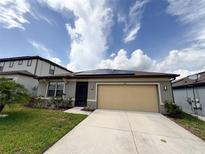 Inviting single-story home featuring a tan garage, a well-manicured lawn, and solar panels against a beautiful sky at 398 Citrus Isle Loop, Davenport, FL 33837