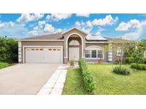 Charming home with an arched entryway, two-car garage, and a beautifully landscaped lawn under a cloudy sky at 5203 Jasmine Trace Ln, Kissimmee, FL 34758