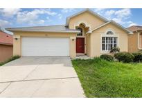 Charming one-story home featuring a two-car garage, red front door, and well-maintained lawn at 1199 Stoneham Dr, Groveland, FL 34736