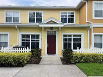 Charming yellow townhome featuring a red front door, white picket fence and lush landscaping at 4010 Santa Maria Dr # 106, Kissimmee, FL 34741