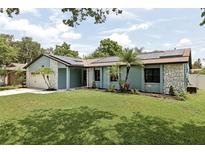 Charming single-story home with a manicured lawn, accented by stone details and solar panels on the roof at 1360 Gladiolas Dr, Winter Park, FL 32792
