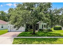 Charming single-story home with a lush green lawn, mature trees, and a brick driveway at 1124 Hidden Blf, Clermont, FL 34711