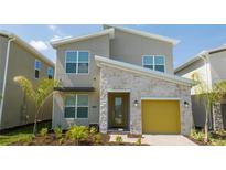 Modern two-story home with a yellow garage door, stone accents, and landscaped yard at 8964 Takeaway Way, Davenport, FL 33896
