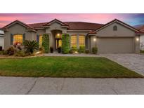 Charming home featuring a red tile roof, manicured lawn and lush landscaping, all illuminated by warm exterior lighting at 2359 Baronsmede Ct, Winter Garden, FL 34787