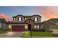 Charming two-story home with a well-manicured lawn, stone accents, and a two-car garage with crimson doors and shutters at 731 Arbor Pointe Ave, Minneola, FL 34715