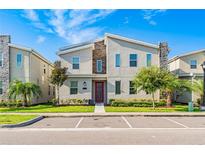 Modern townhouse with a red door, stone accents, a well-manicured lawn, and dedicated parking spaces at 4530 Narrative Ln, Kissimmee, FL 34746
