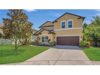 Two-story tan home featuring a well-manicured lawn and attached two-car garage at 15659 Carina Dr, Orlando, FL 32828