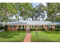 Charming brick home featuring a manicured lawn, brick walkway, and mature trees draped with Spanish moss at 2500 Lake Shore Dr, Orlando, FL 32803