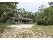 Ranch-style home featuring a long covered front porch, gravel driveway, mature trees, and natural landscaping at 26586 Se Highway 42, Umatilla, FL 32784