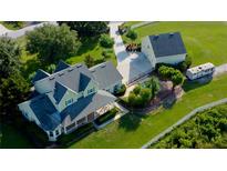 Expansive aerial view of a large, light green house with a detached garage, pool, and green lawn at 10809 Arrowtree Blvd, Clermont, FL 34715
