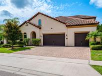 Beautiful home featuring a red tile roof, a three-car garage and a lovely brick driveway and tropical landscaping at 8047 Chilton Dr, Orlando, FL 32836