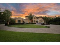 Stunning Mediterranean-style home with circular driveway, lush lawn and professional landscaping against a backdrop of a dramatic sunset at 11103 Bridge House Rd, Windermere, FL 34786