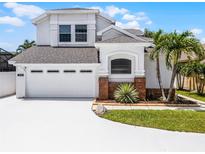 Two story home featuring an attached two car garage, neutral paint, decorative brick detail, and tropical landscaping at 14423 Tambourine Dr, Orlando, FL 32837